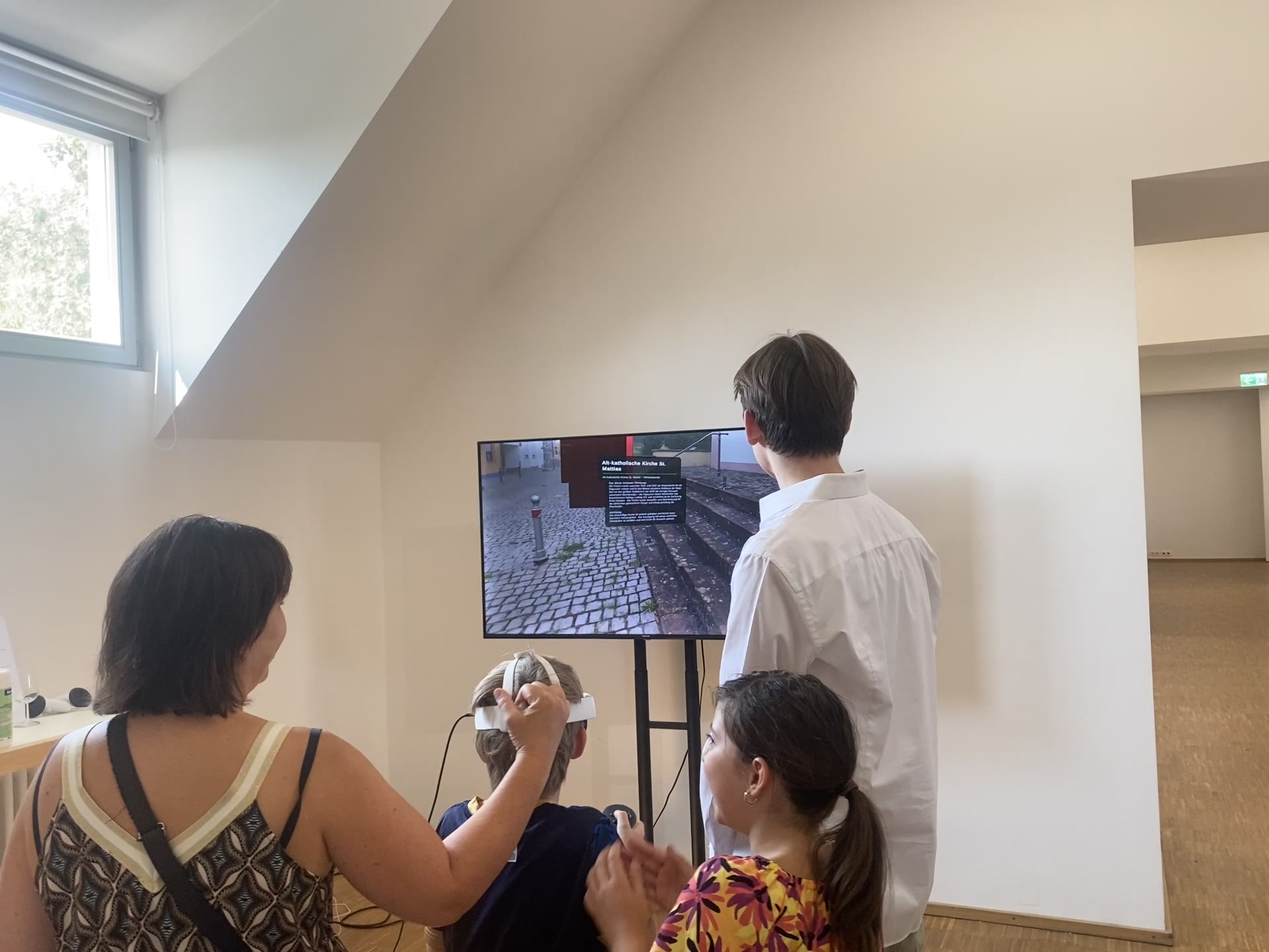 A visitor using the VR headset while the exhibition monitor shows the real-time scene